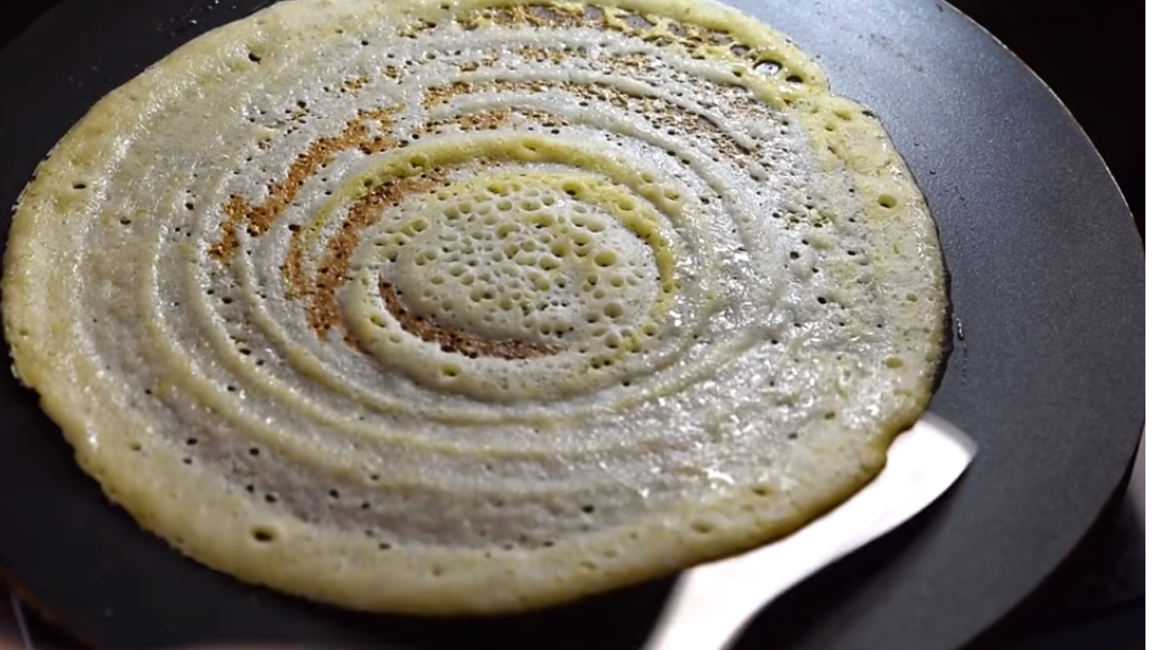 Golden brown suji dosa being cooked on a hot tava with a spatula