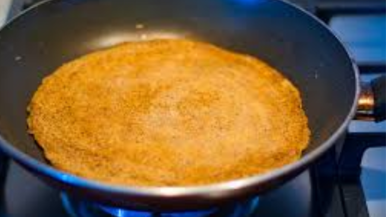 Lentil pancake cooking in a greased pan with beetroot slices on top