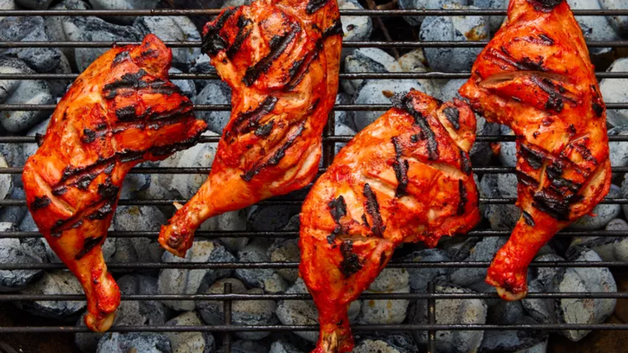 Tandoori chicken pieces cooking on an outdoor grill with char marks